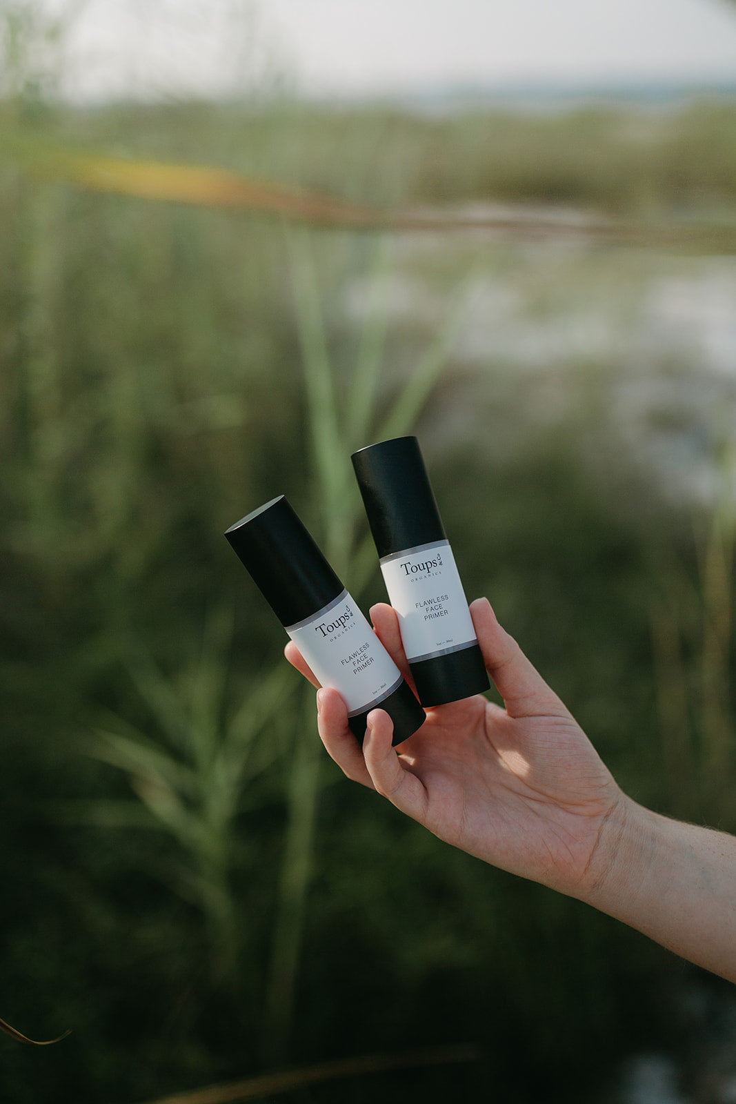 woman-holding-two-makeup-primers-against-beach-background