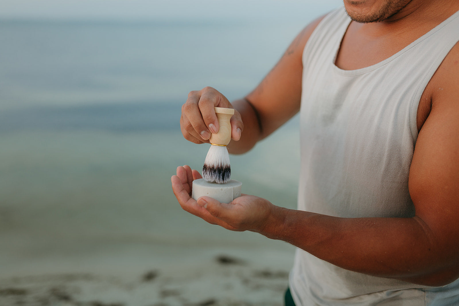 man-using-shave-brush-and-tallow-soap-with-beach-background