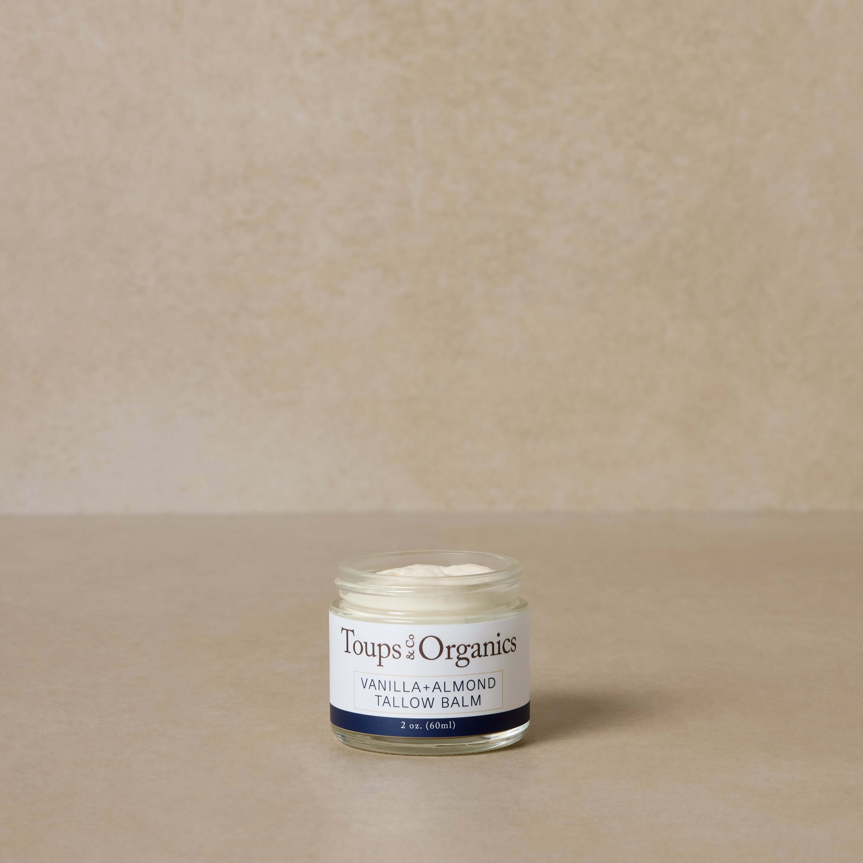 small-vanilla-and-almond-tallow-balm-jar-displayed-against-brown-background