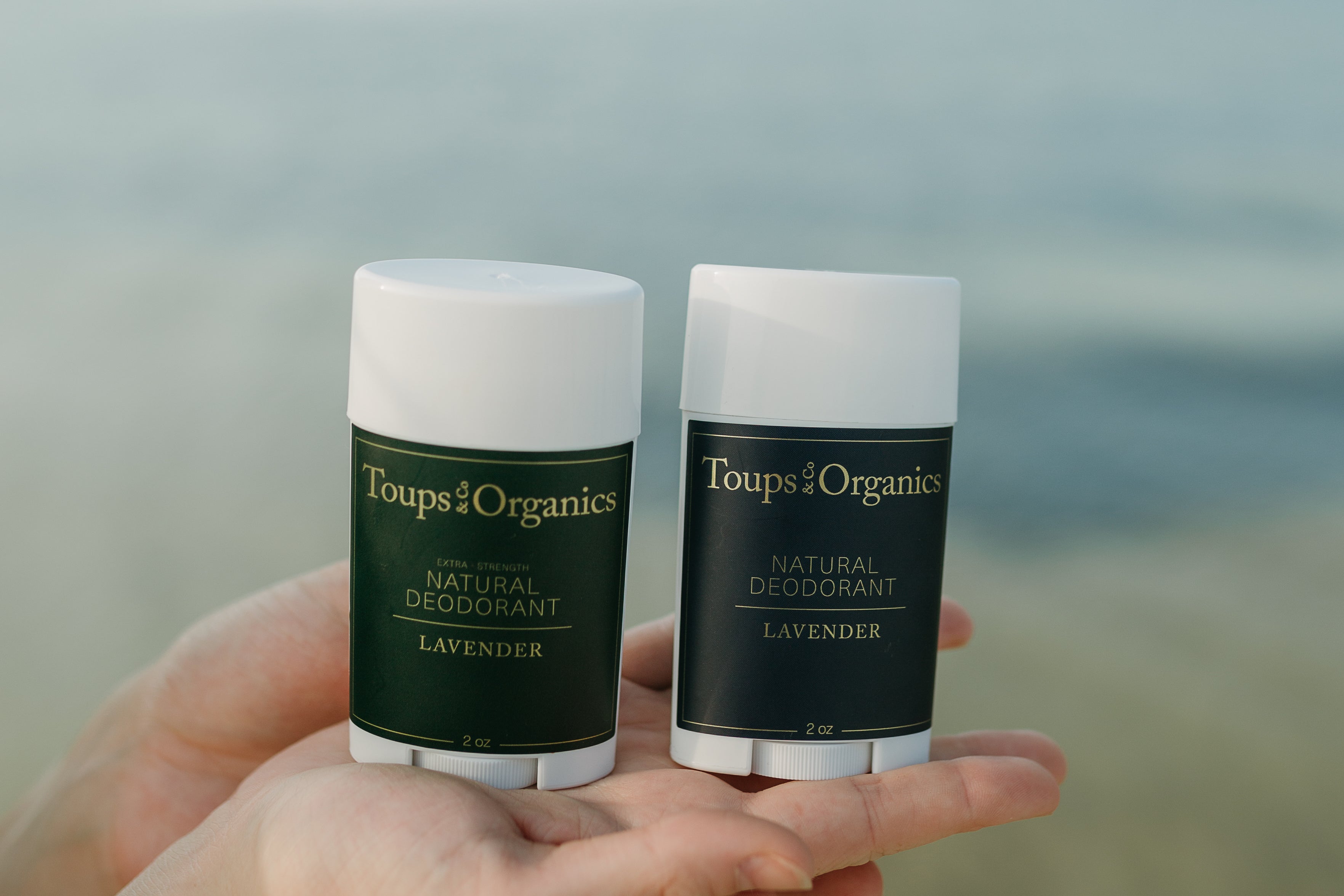 woman-holding-two-tubes-of-natural-deodorant-against-ocean-background