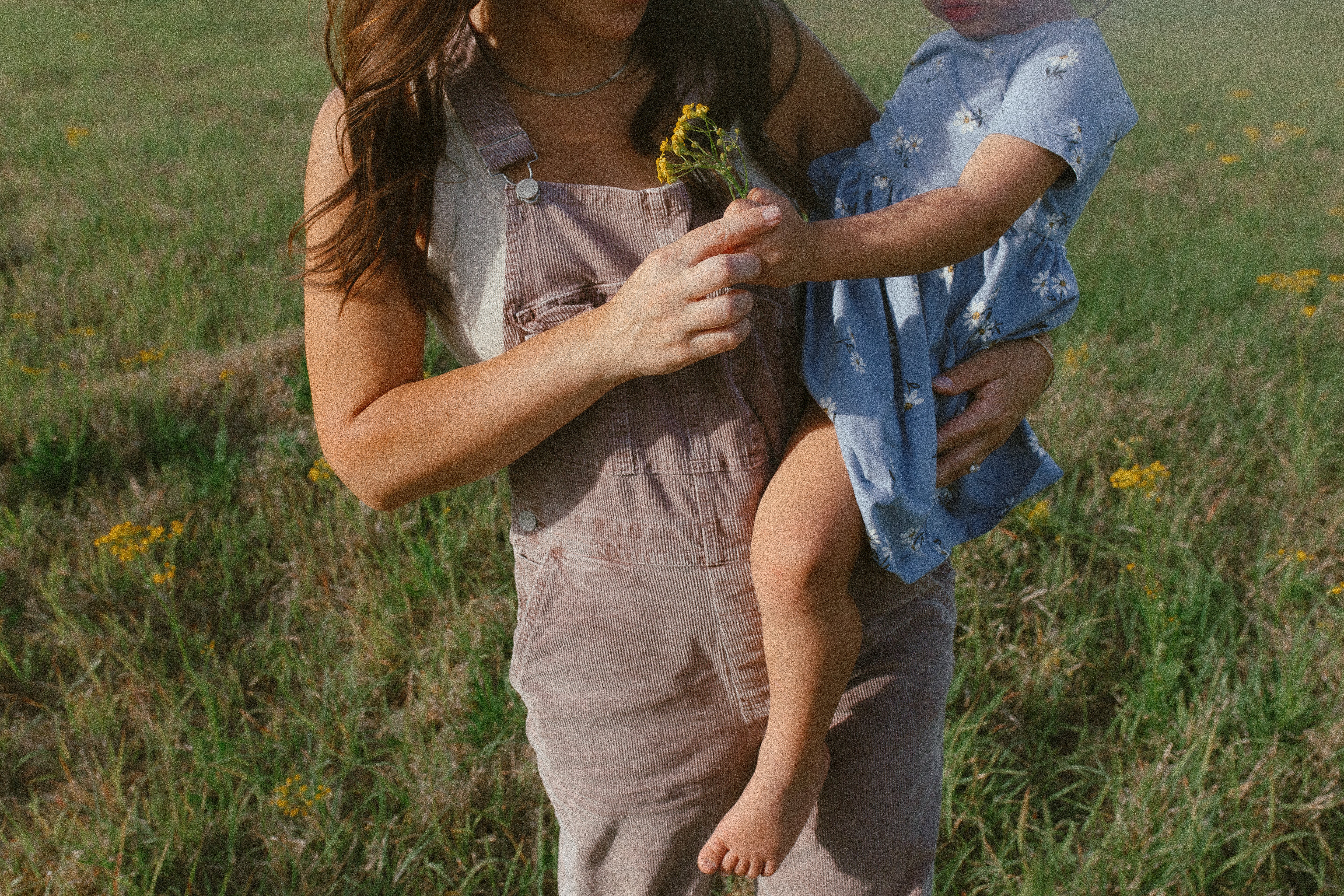 Toups & Co mom holding toddler in a wildflower field, sharing a quiet postpartum bonding moment.