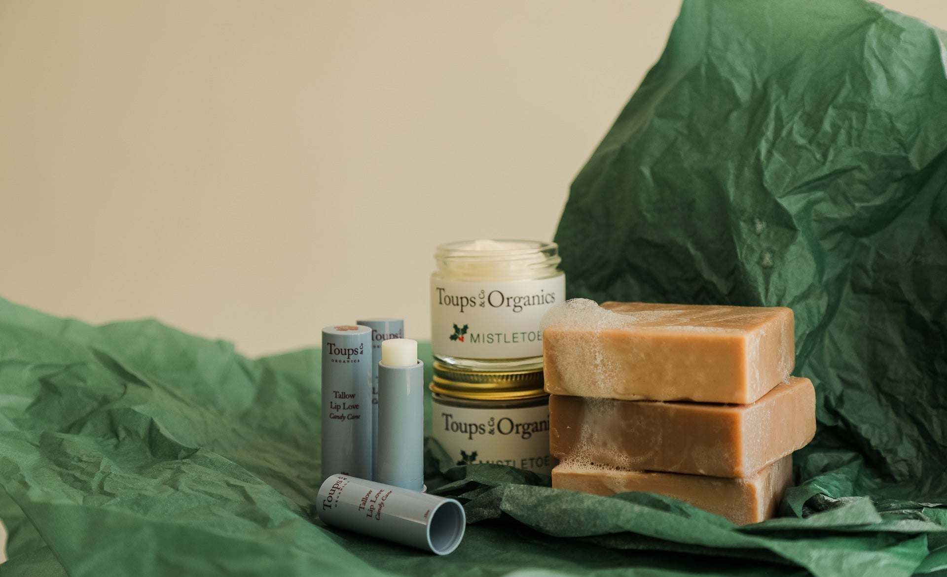 Green stocking embroidered with Mom beside jars labeled Toups & Co Organics Mistletoe and tubes labeled Candy Cane on a marble surface.