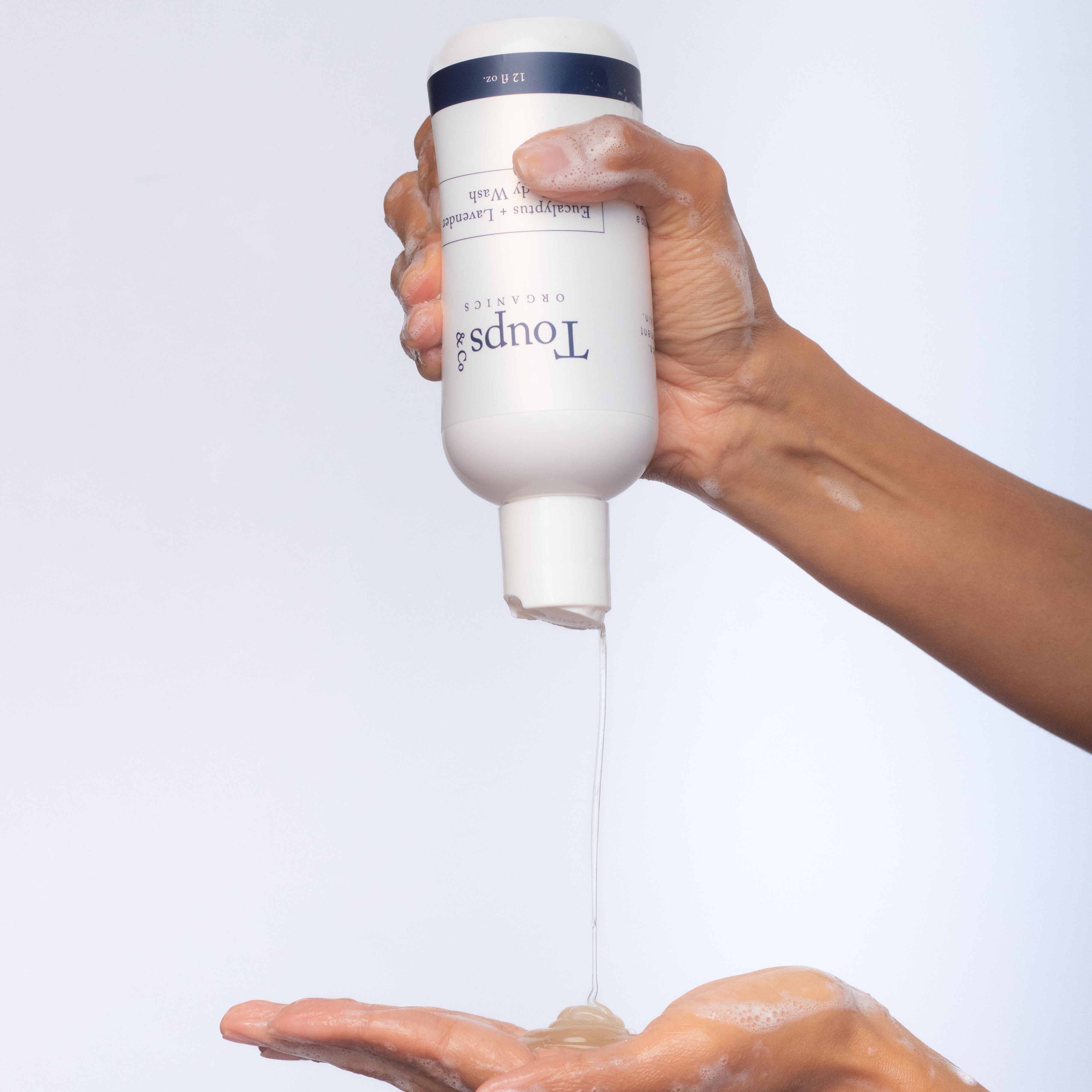 A person dispenses Toups and Co Organics Body Wash onto their palm against a plain white background.