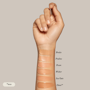 A raised arm displays six Sample Set - Liquid Foundation shades by Toups and Co Organics swatched on the forearm, labeled top to bottom: Brulee, Praline, Pecan, Wicker, Sea Oats, and Dune. Made with all-natural ingredients.