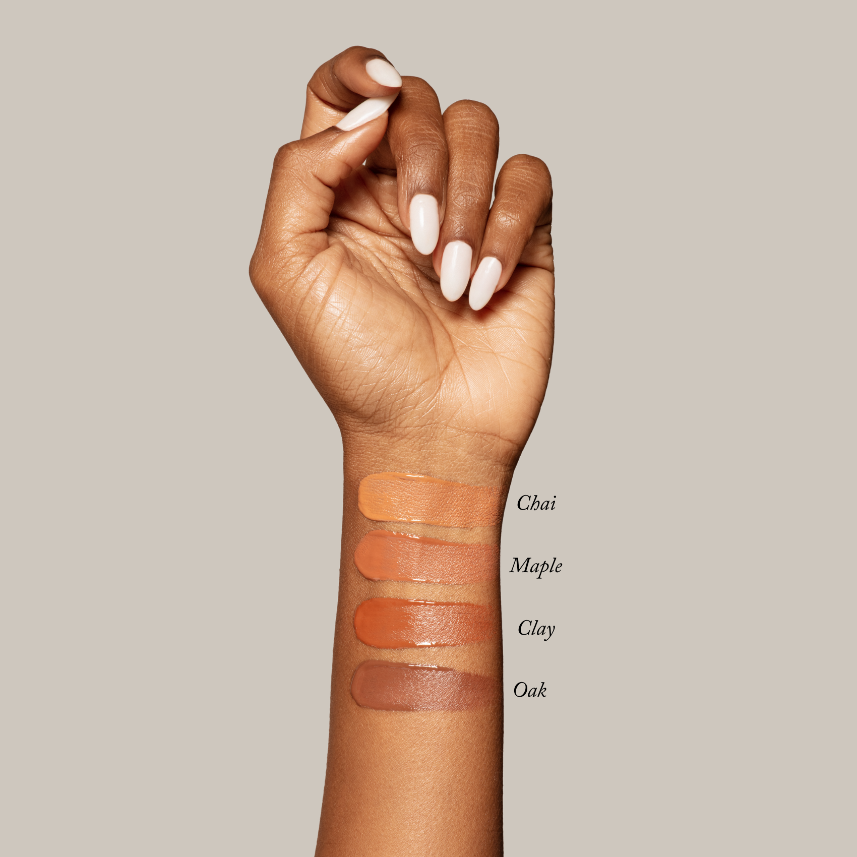 A hand displays four Toups and Co Organics Sample Set - Liquid Foundation swatches—Chai, Maple, Clay, and Oak—on the inner forearm against a plain beige background.