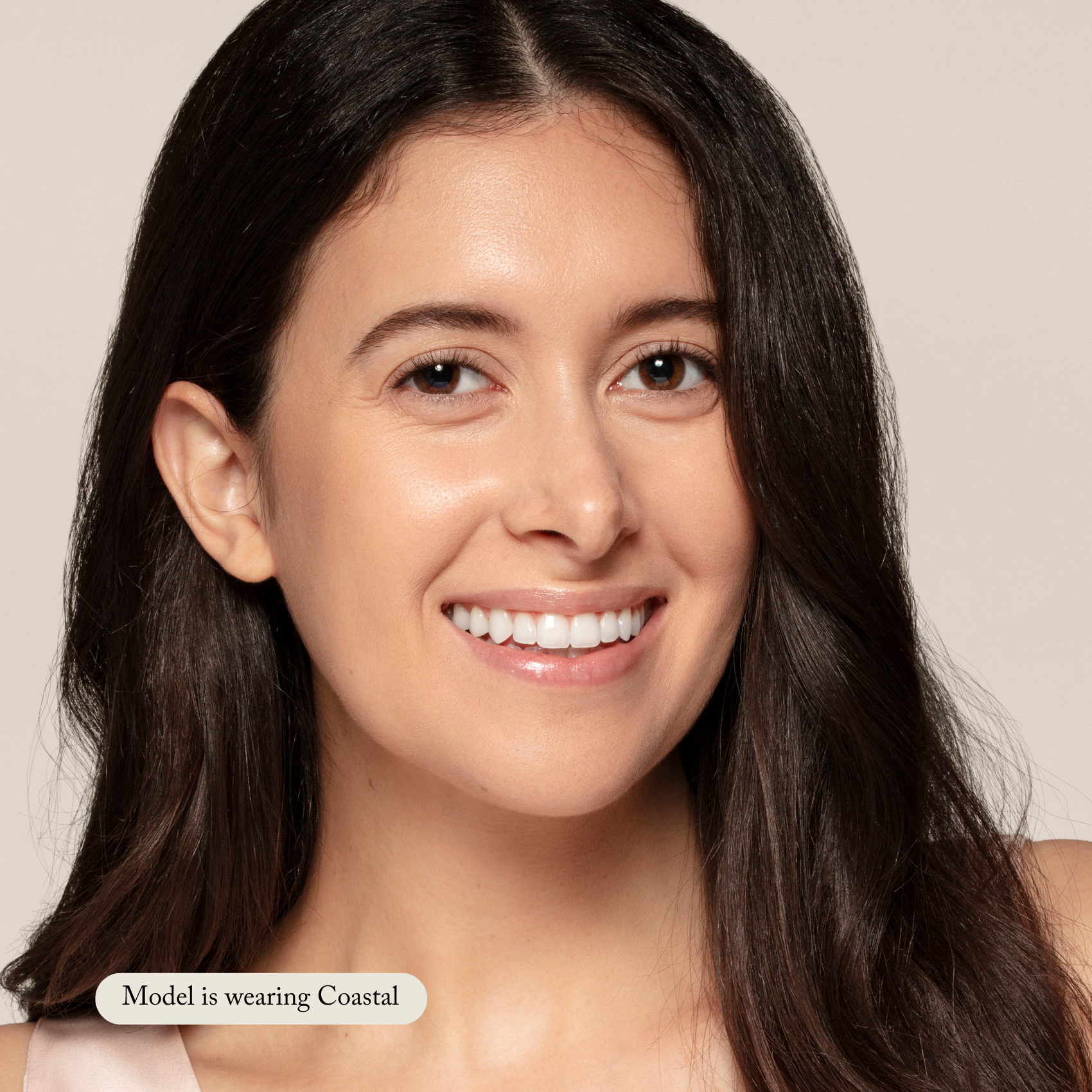 A woman with long dark hair smiles at the camera against a plain backdrop, radiating a natural glow. A label reads: Model is wearing Liquid Foundation by Toups and Co Organics, ideal for sensitive skin.