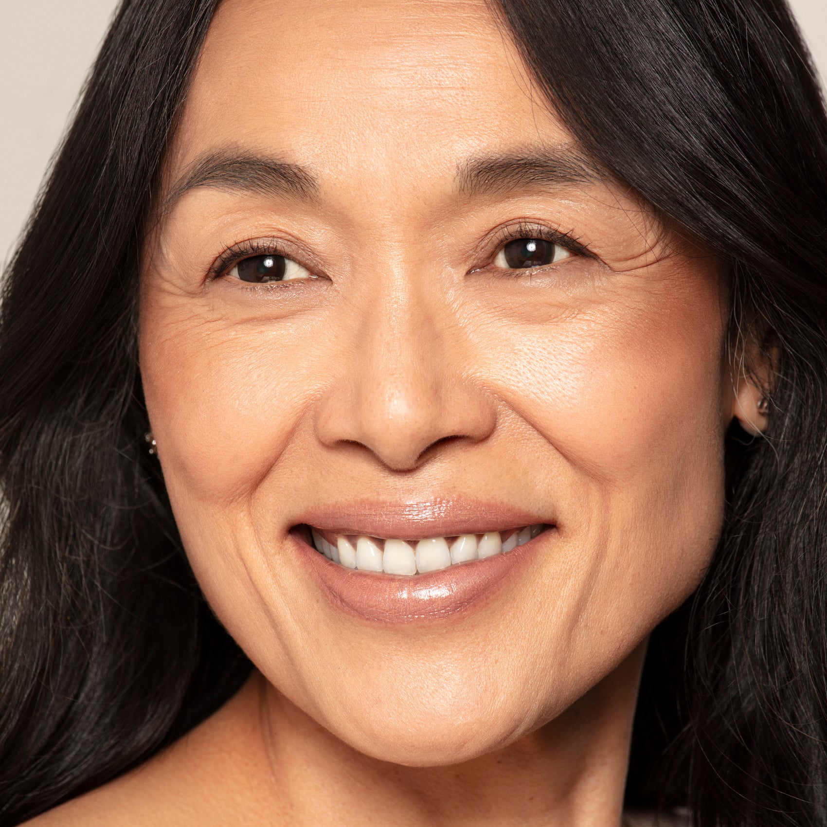 A woman with long dark hair, clear skin, and a natural smile looks slightly right, highlighting her sun-kissed glow created with Toups and Co Organics Bronzer.