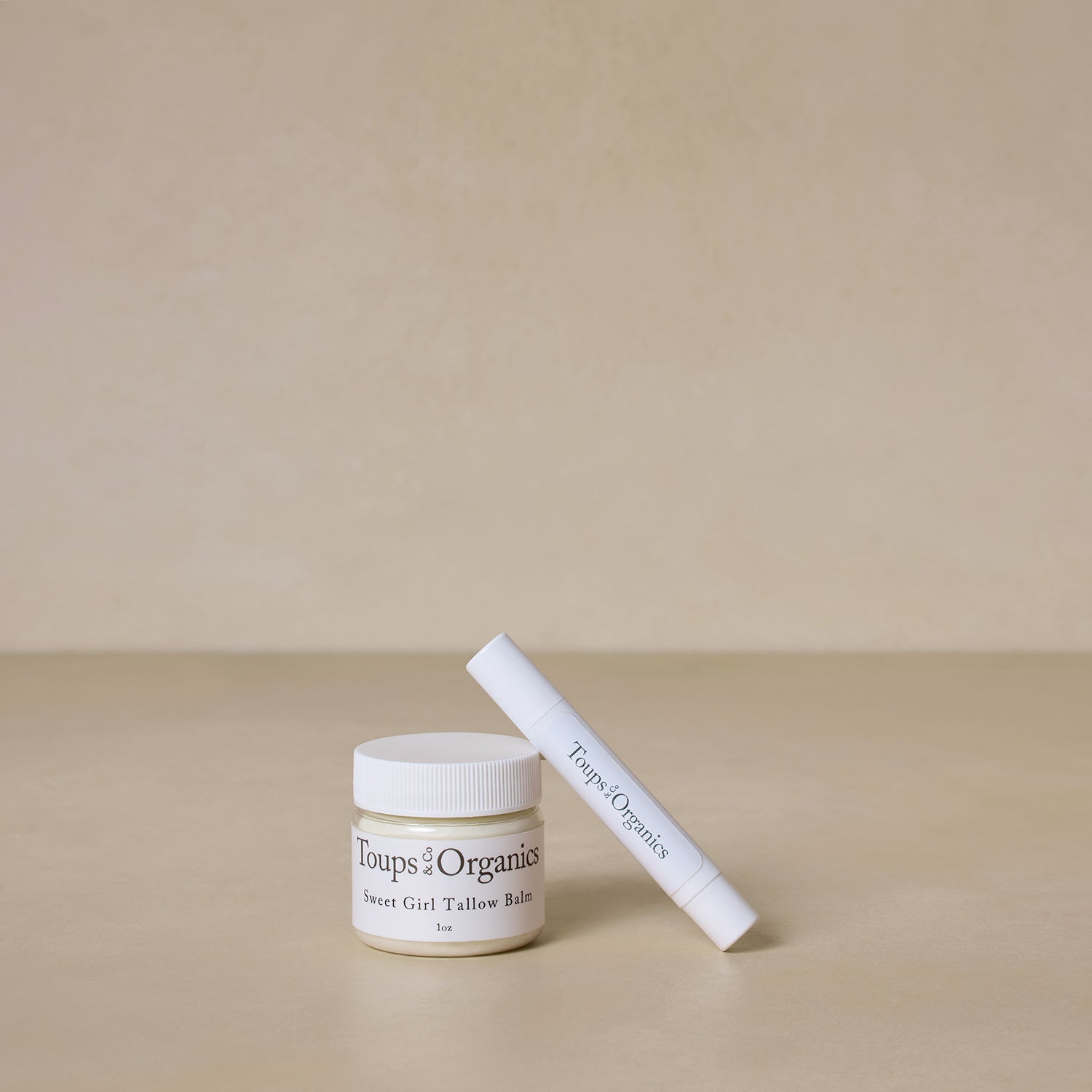 A jar labeled Toups and Co Organics The Bridesmaid Edit and a white cylindrical tube labeled Toups and Co Organics on a neutral surface.