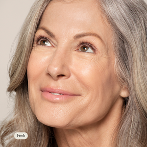 Close-up of an older woman with gray hair and smooth skin, smiling softly against a neutral background, highlighting the natural hydration benefits of Toups and Co Organics Concealer for sensitive skin.