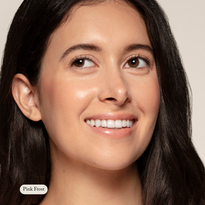 A woman with long dark hair and clear skin smiles, wearing subtle makeup and a touch of Toups and Co Organics Cream Cheek Tint for a natural glow. The neutral background features the label Pink Frost in the corner.