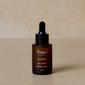 A brown glass dropper bottle labeled Toups and Co Organics Blushing Bridal Set sits on a neutral beige surface—perfect for wedding-day skincare or adding to your bridal beauty routine.