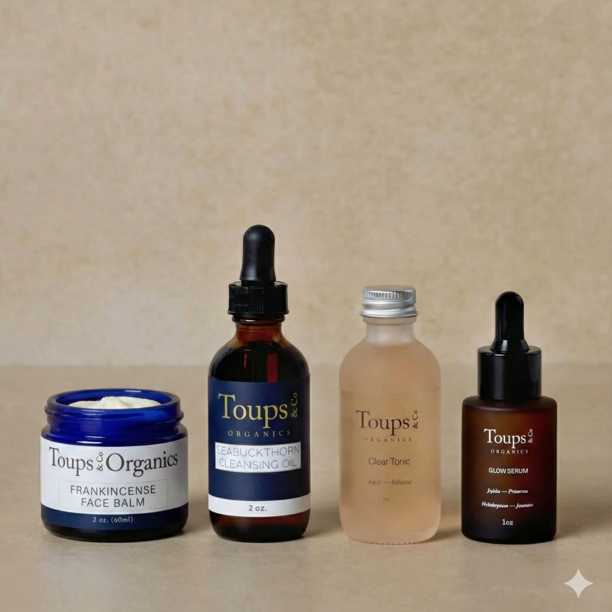 The Toups and Co Organics Skincare Starter Set features four nontoxic products—a face balm, cleansing oil, tonic, and facial serum—displayed on a beige surface in various containers for clean beauty care.