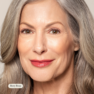 Close-up of an older woman with long gray hair and natural makeup, wearing Toups and Co Organics Organic Lip Gloss in a deep berry shade, featuring a moisturizing formula and safe, nontoxic ingredients.