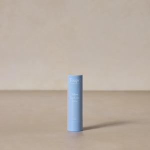 A light blue tube of Toups and Co Organics Tallow Lip Love stands upright on a neutral beige surface with a matching background—ideal for soothing chapped lips.