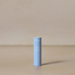 A light blue tube of Toups and Co Organics Tallow Lip Love hydrating lip balm stands upright on a beige surface against a neutral background.