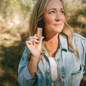 A woman holding a bottle of Toups & Co. liquid foundation.