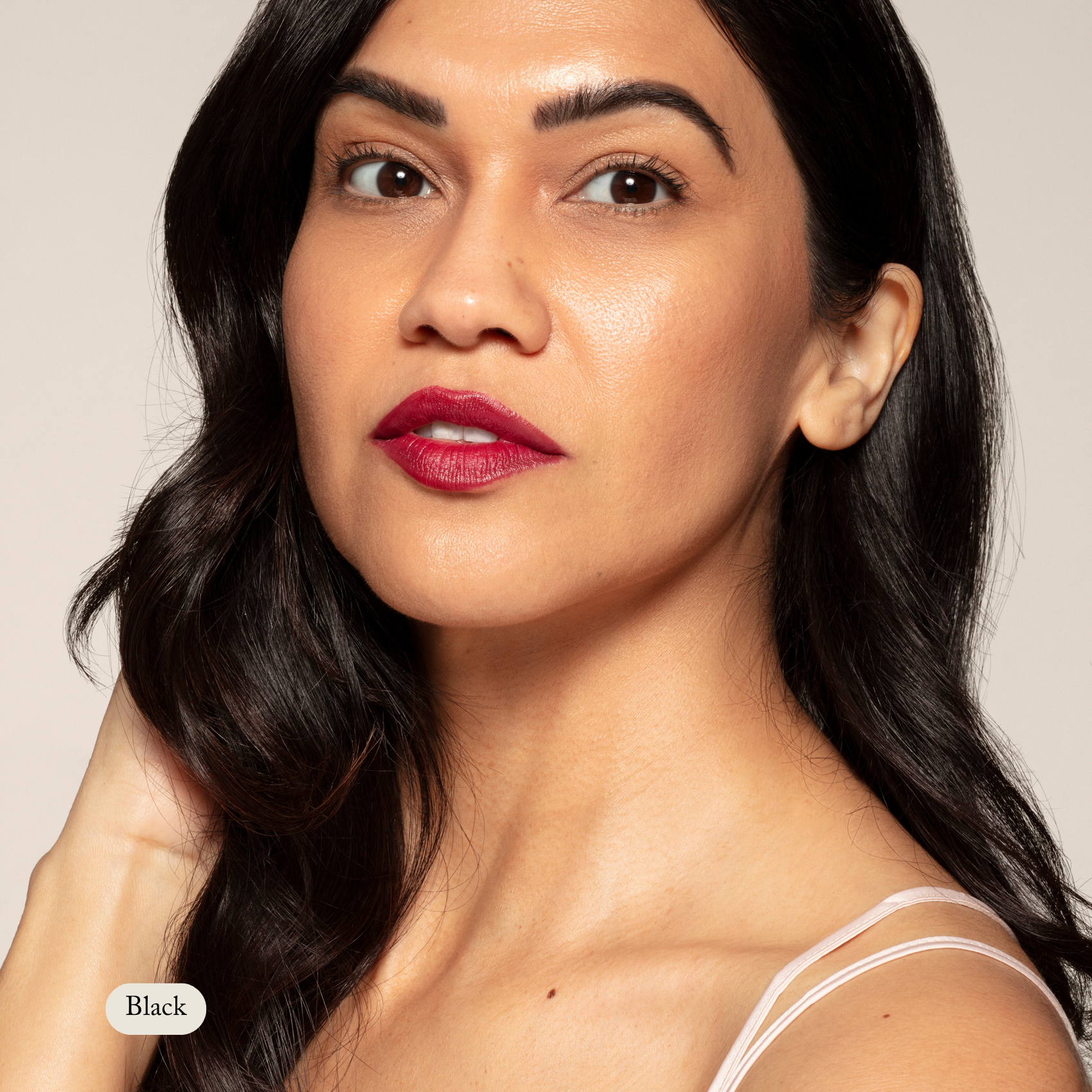Woman with long, dark hair and bold red lipstick gazes at the camera, her lashes defined by Toups and Co Organics Long Lash Mascara, wearing a white spaghetti strap top against a neutral background.