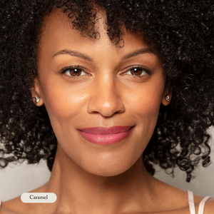 A woman with curly dark hair and caramel-toned skin smiles softly at the camera, wearing earrings and a natural look accentuated by Toups and Co Organics Mineral Makeup for a fresh, non-toxic finish.
