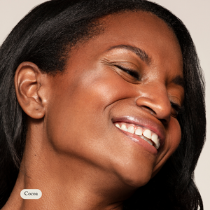 Close-up of a smiling woman with medium to dark skin and glowing complexion. Cocoa shade label highlights the benefits of Toups and Co Organics Mineral Makeup—non-toxic and healthy for your skin.