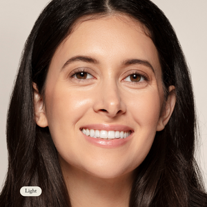 A woman with long dark hair smiles at the camera against a neutral background. A label reading Light highlights Toups and Co Organics Mineral Makeup, a non-toxic formula with natural SPF for radiant, healthy-looking skin.