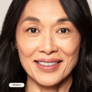 A close-up of a middle-aged woman with long dark hair and a light complexion, smiling at the camera against a plain background. The “Medium” label highlights her flawless look achieved with Toups and Co Organics Mineral Makeup.