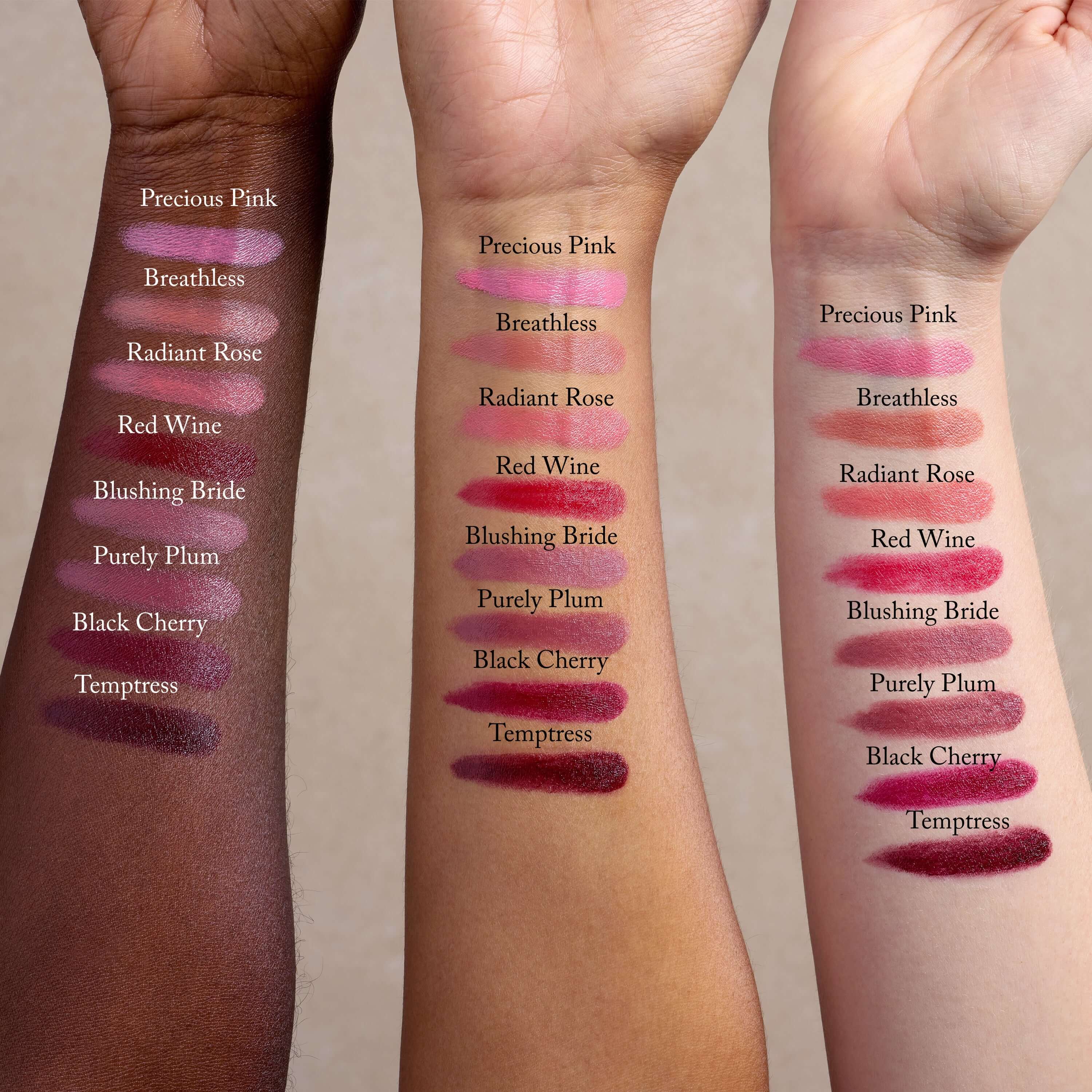 Three arms of varying skin tones show swatches of Toups and Co Organics Nourishing Lipstick, enriched with hydrating butters and antioxidants. Shades from top to bottom: Precious Pink, Breathless, Radiant Rose, Red Wine, Blushing Bride, Purely Plum, Black Cherry, Temptress.