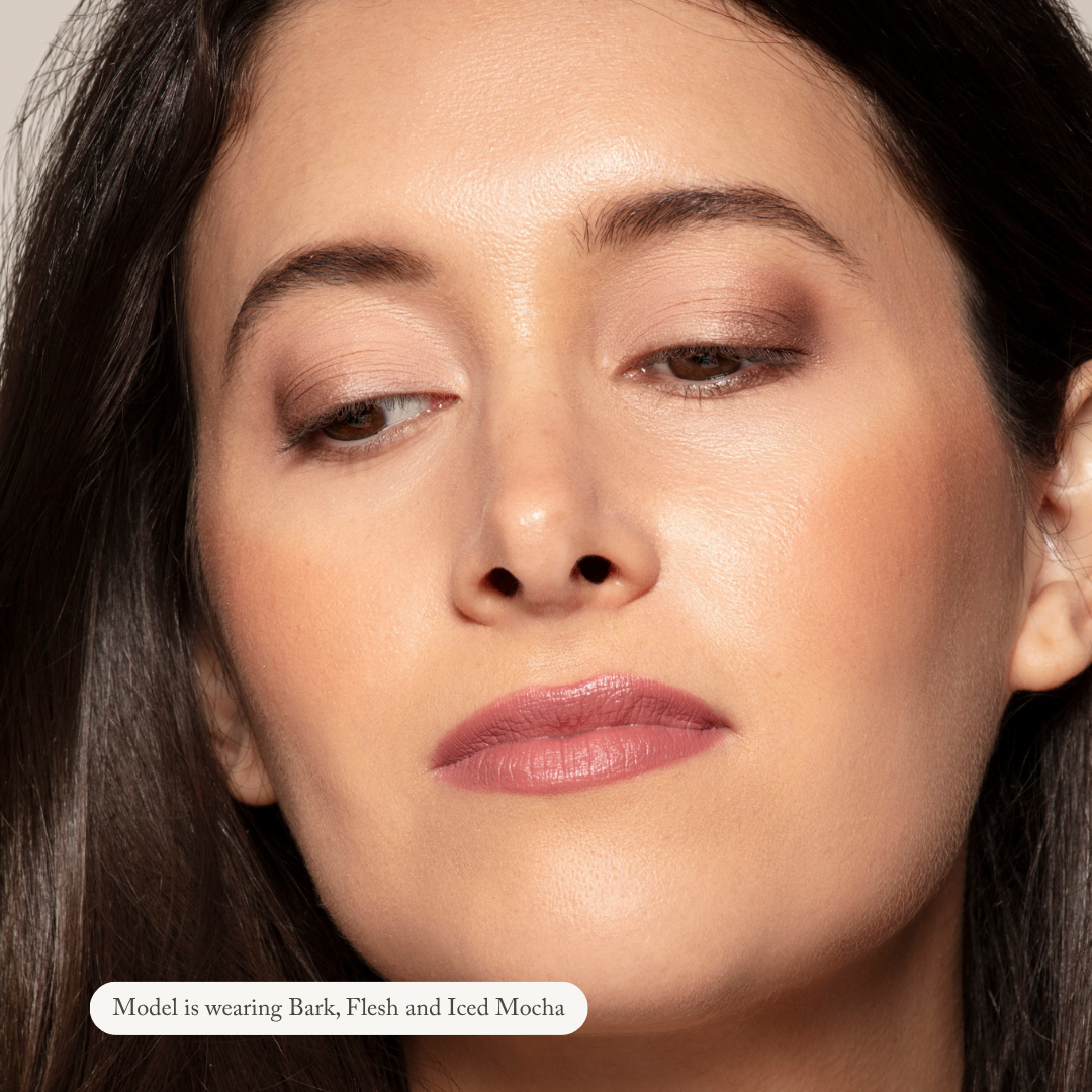 A woman with smooth, medium skin tone and brown hair wears natural-looking brown and mauve Toups and Co Organics Natural Eyeshadow Singles on her eyelids, cheeks, and lips. Text reads: Model is wearing Natural Eyeshadow Singles.