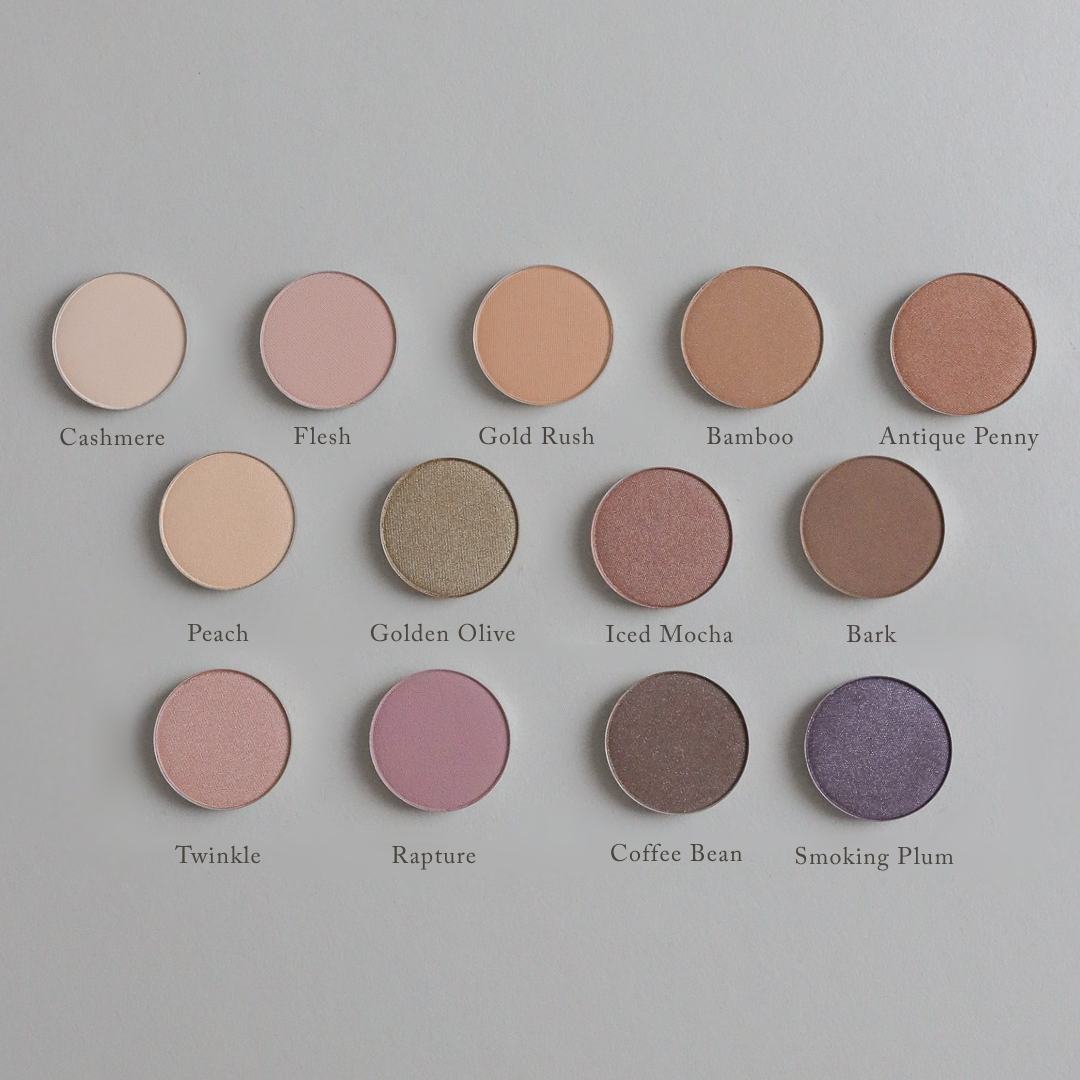 Twelve round, richly pigmented Toups and Co Organics Natural Eyeshadow Singles, each labeled with names in various shades, are arranged in rows on a tan background. This magnetic eyeshadow palette allows you to customize your look with clean, single pans for effortless, vibrant color every time.