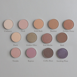 Twelve round, richly pigmented Toups and Co Organics Natural Eyeshadow Singles, each labeled with names in various shades, are arranged in rows on a tan background. This magnetic eyeshadow palette allows you to customize your look with clean, single pans for effortless, vibrant color every time.