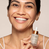 Woman smiling and holding a dropper bottle labeled Toups and Co Organics Reparative Serum with bakuchiol and amino acids close to her face.
