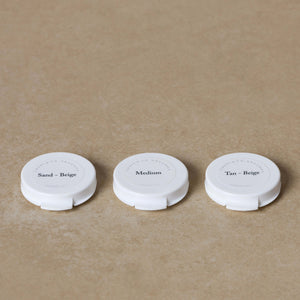 Three white compacts labeled Sand-Beige, Medium, and Tan-Beige from Toups and Co Organics Sample Set - Mineral Foundation are arranged on a beige surface to help you find your perfect mineral foundation shade.