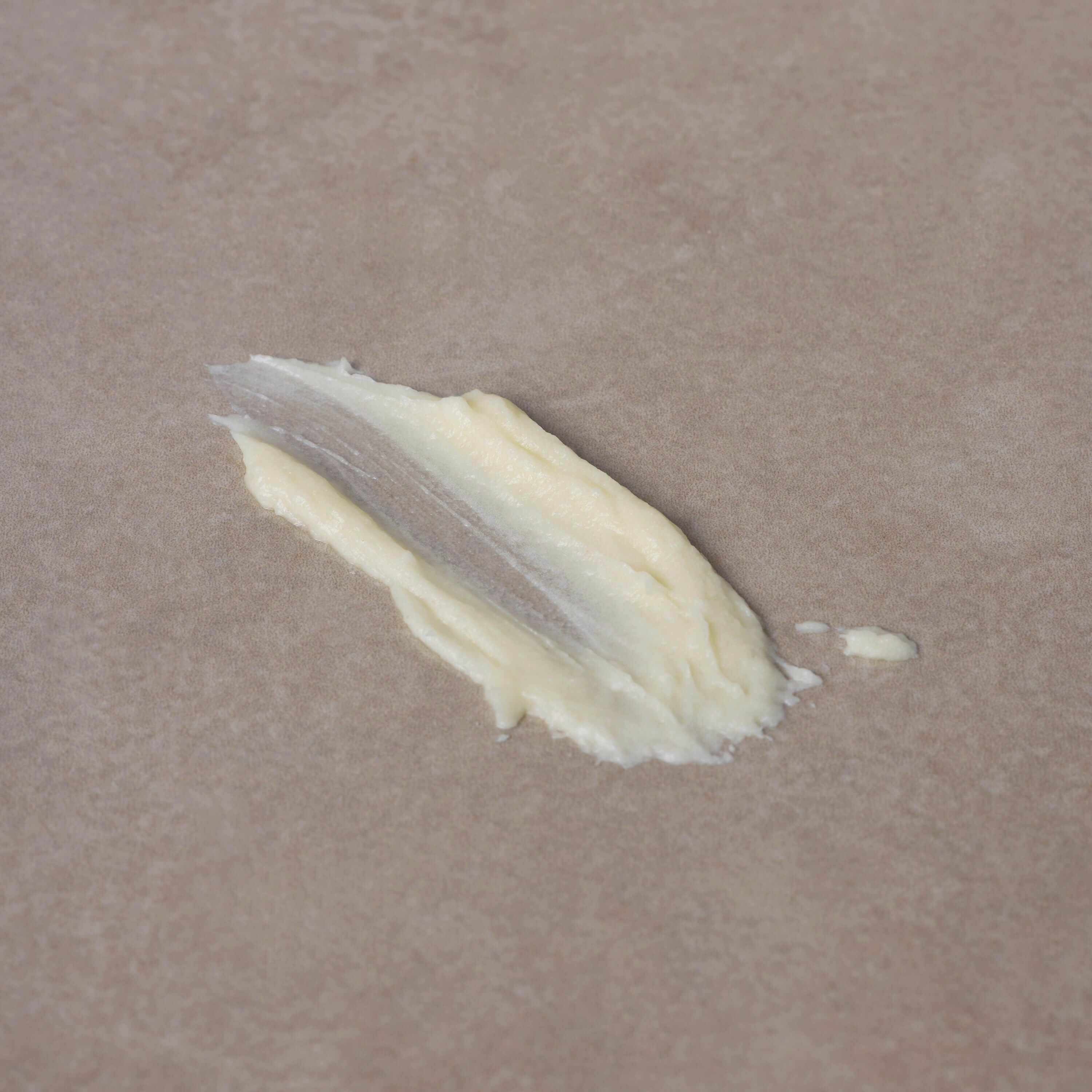 A small smear of Toups and Co Organics Tallow Balm - Vanilla + Almond, made from nourishing grass-fed tallow, on a sheet of parchment paper.