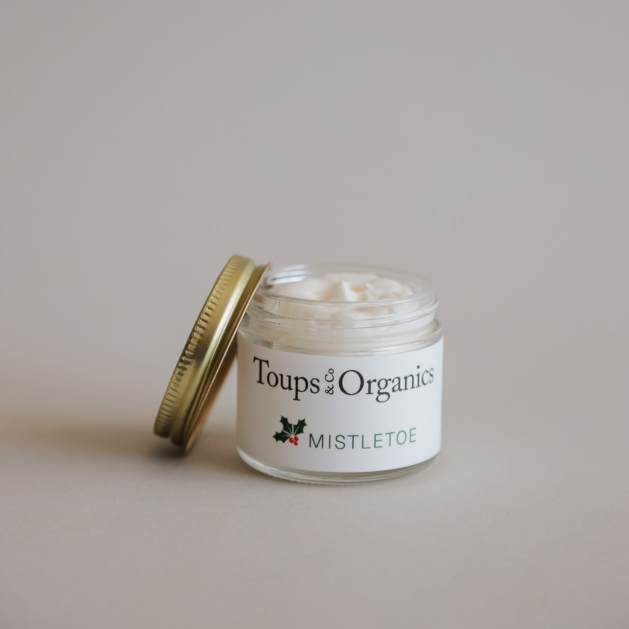 A small glass jar with a gold lid from Toups and Co Organics’ Merry and Bright Gift Set, partially opened to reveal white tallow balm—ideal for natural skincare or gifting during the holidays.