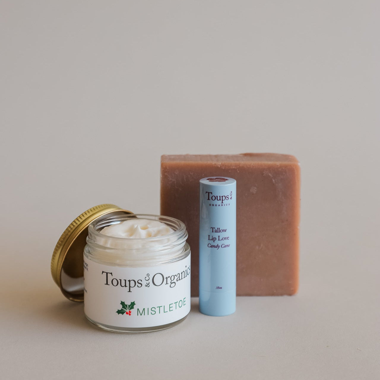 The Merry and Bright Gift Set by Toups and Co Organics includes mistletoe cream, Tallow Lip Love Candy Cane lip balm, and a bar of soap, all arranged beautifully on a neutral background for a perfect natural skincare holiday gift.