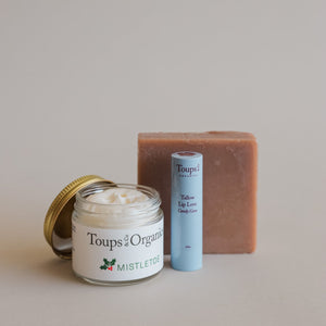 The Merry and Bright Gift Set by Toups and Co Organics includes mistletoe cream, Tallow Lip Love Candy Cane lip balm, and a bar of soap, all arranged beautifully on a neutral background for a perfect natural skincare holiday gift.