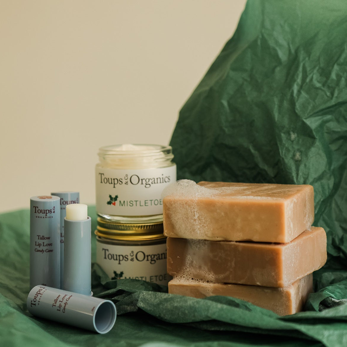 The Merry and Bright Gift Set by Toups and Co Organics includes several soaps, two tallow balms, and three lip balms on green tissue—perfect as a natural skincare holiday gift.