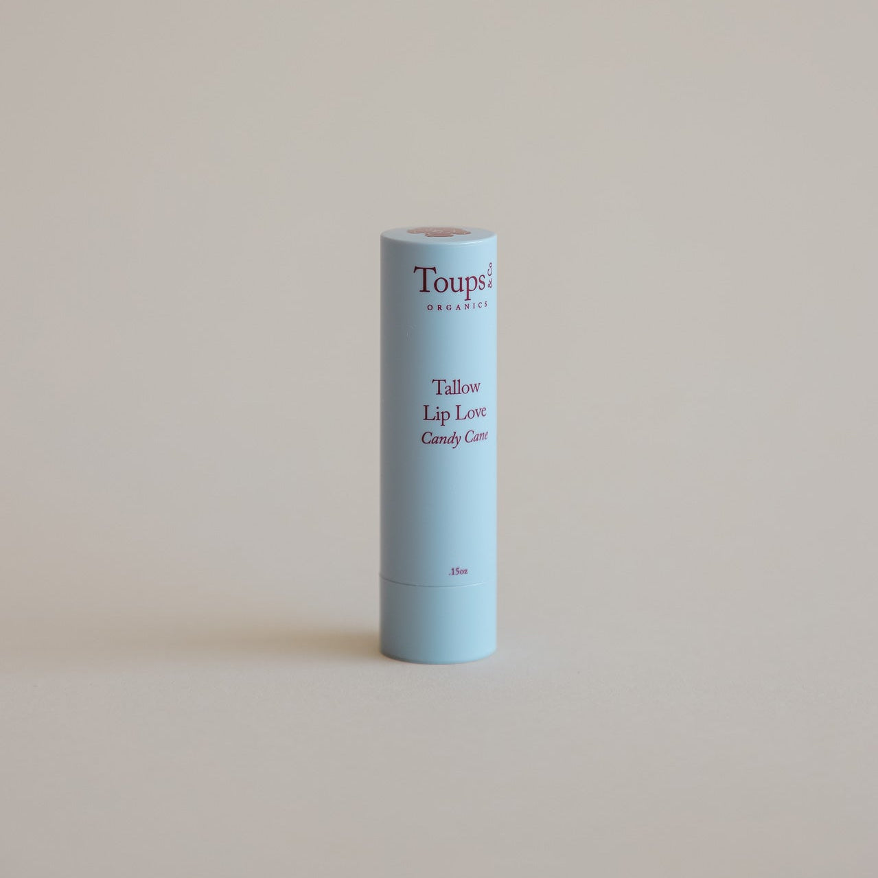 A light blue tube of Toups and Co Organics Merry and Bright Gift Set Tallow Lip Love Candy Cane balm stands upright on a plain beige background—ideal for natural skincare or holiday gifting.
