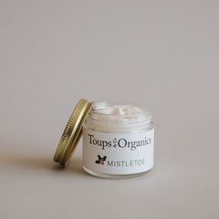 A glass jar of Toups and Co Organics Mistletoe Balm with a gold lid, filled with creamy white balm, sits against a plain background—an ideal Christmas gift.