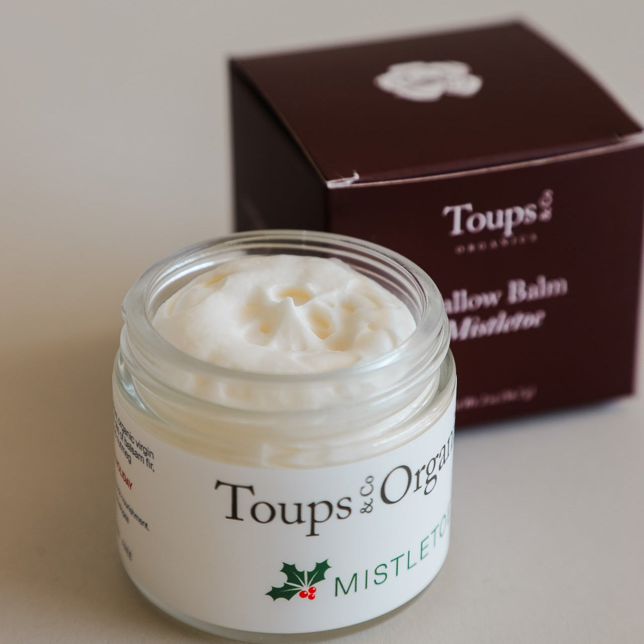 An open jar of Toups and Co Organics Mistletoe Balm sits before its maroon box on a light surface—an ideal choice for thoughtful Christmas gifts.