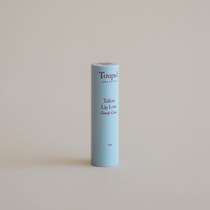 A light blue tube of Toups and Co Organics Candy Cane Lip Love tallow lip balm stands upright on a plain beige background.