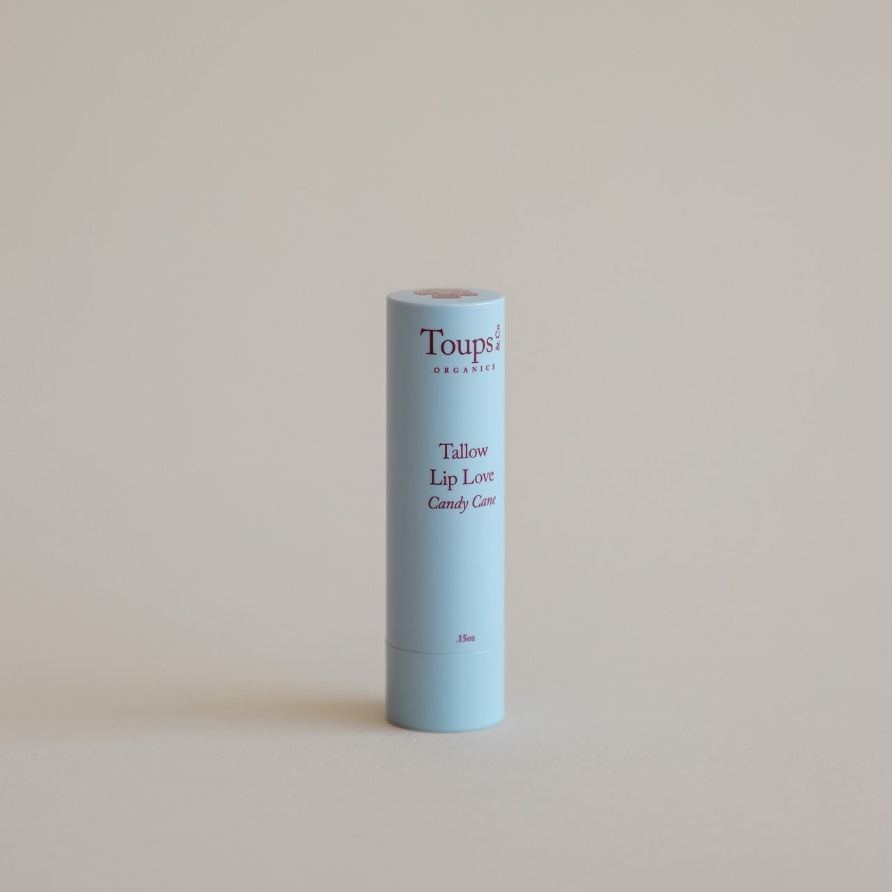 A light blue tube of Toups and Co Organics Candy Cane Lip Love stands upright against a plain beige background.