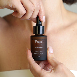 A person holding a bottle of Toups and Co Organics Clean Serum Set with a dropper, positioned in front of their bare upper chest.