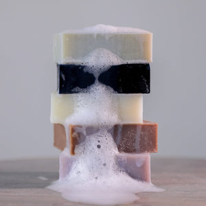 A stack of five colorful Everything Bar soap bars from Toups and Co Organics, made with organic coconut oil, rests on a smooth surface as foamy suds cascade down the center.