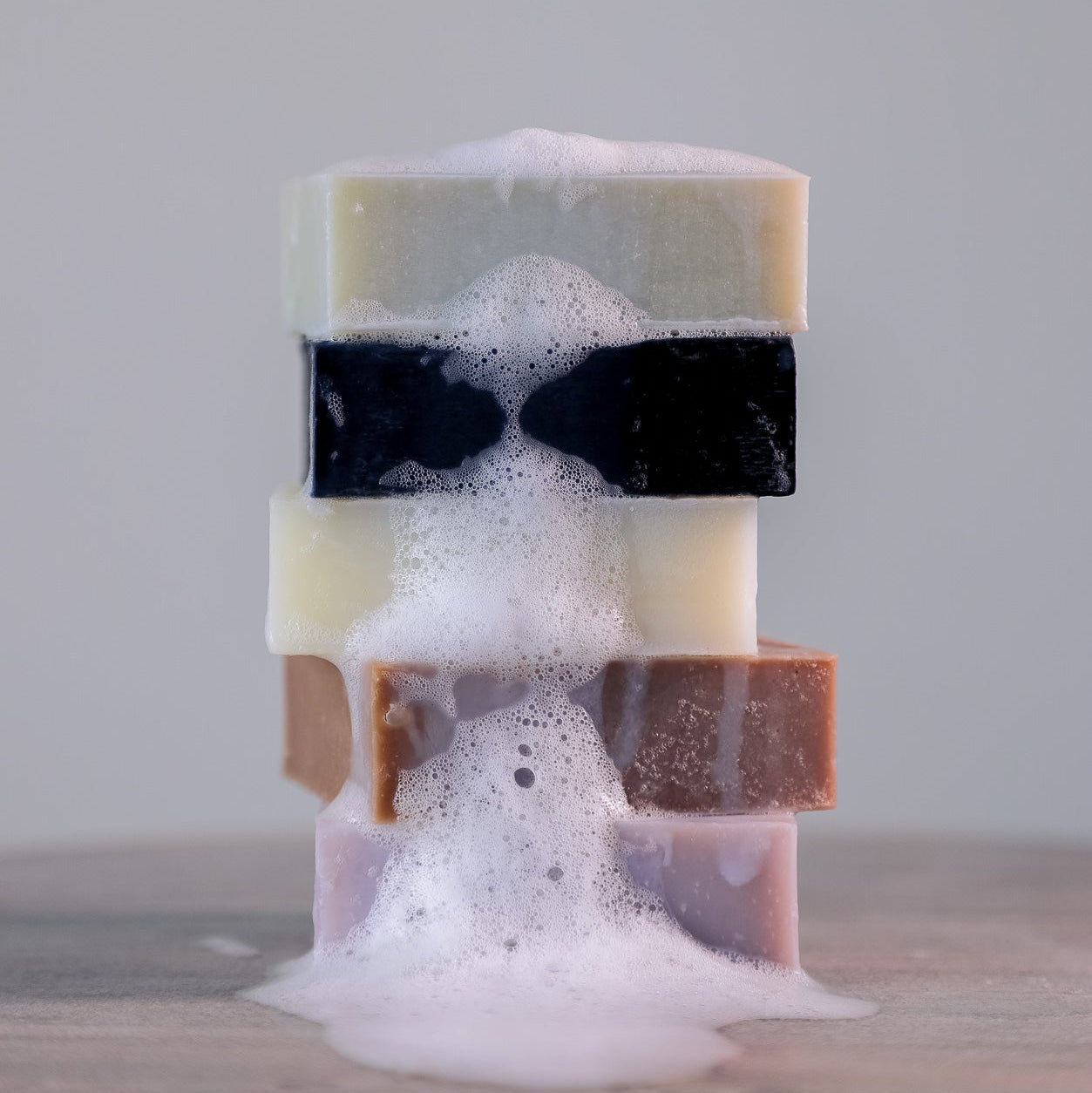 A stack of five colorful Everything Bar soap bars from Toups and Co Organics, made with organic coconut oil, rests on a smooth surface as foamy suds cascade down the center.