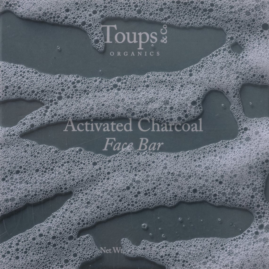 Gray bar of soap with white suds, labeled Toups and Co Organics Activated Charcoal Face Bar in white text, crafted with activated bamboo charcoal and nourishing grass-fed tallow.