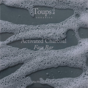 Gray bar of soap with white suds, labeled Toups and Co Organics Activated Charcoal Face Bar in white text, crafted with activated bamboo charcoal and nourishing grass-fed tallow.
