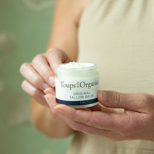 A person holds an open jar of Toups and Co Organics Tallow Balm – Original, revealing the white balm inside—perfect for sensitive skin and all-over moisture.