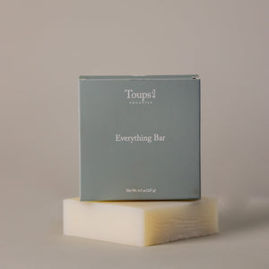 A gray box labeled Toups and Co Organics Everything Bar rests atop an off-white bar made with organic coconut oil, all set against a neutral background.