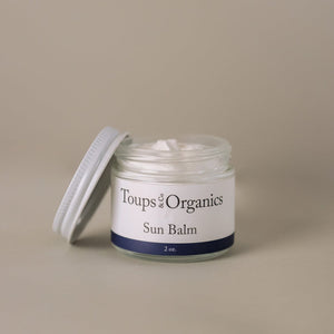 A small glass jar labeled Toups and Co Organics Sun Balm, with a white screw-on lid set aside, holds a white cream formulated with natural mineral sunscreen ingredients such as non-nano zinc oxide.