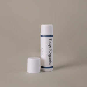 An upright white tube of the Toups and Co Organics Sun Stick is displayed with its cap beside it on a plain beige background, delivering effective sun protection and nourishing skincare.